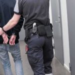 Security officer escorts handcuffed person down hallway