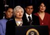 Summit Sparks Major Online Feud Federico Peña stands behind a woman speaking at a podium with the presidential seal