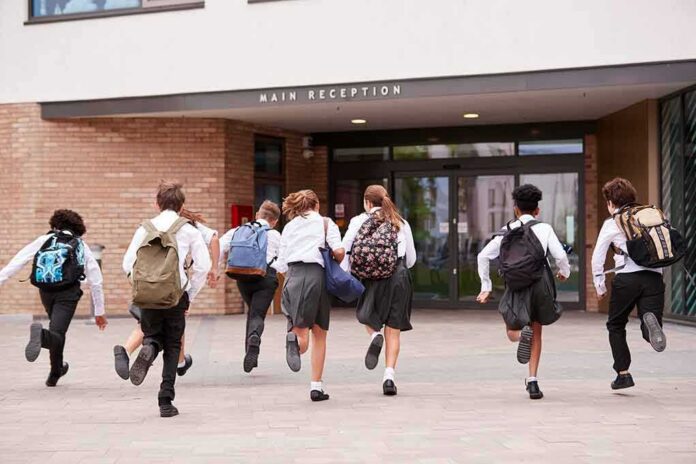 shutterstock_1195675999-1 Students in uniforms running toward a school entrance