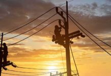 Utility workers on power poles at sunset