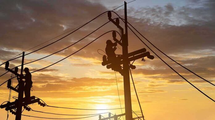 Utility workers on power poles at sunset
