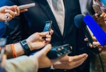 businessperson in suit surrounded by microphones and recorders