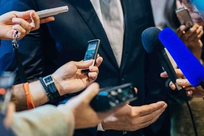 shutterstock_471987556-1 businessperson in suit surrounded by microphones and recorders