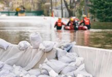 East Coast Braces for Nor’easter Sandbags stacked near a flooded street with rescue workers in a boat