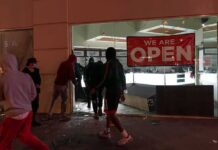 LA Shop Owner Pistol-Whipped in Daylight Robbery People outside a storefront with broken glass at night