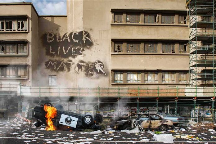 Burning overturned police car in front of a damaged building