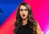 Explosive Attack: Controversial Campaign Ad Woman with glasses speaking on stage with colorful backdrop