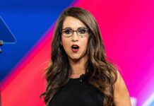 Explosive Attack: Controversial Campaign Ad Woman with glasses speaking on stage with colorful backdrop